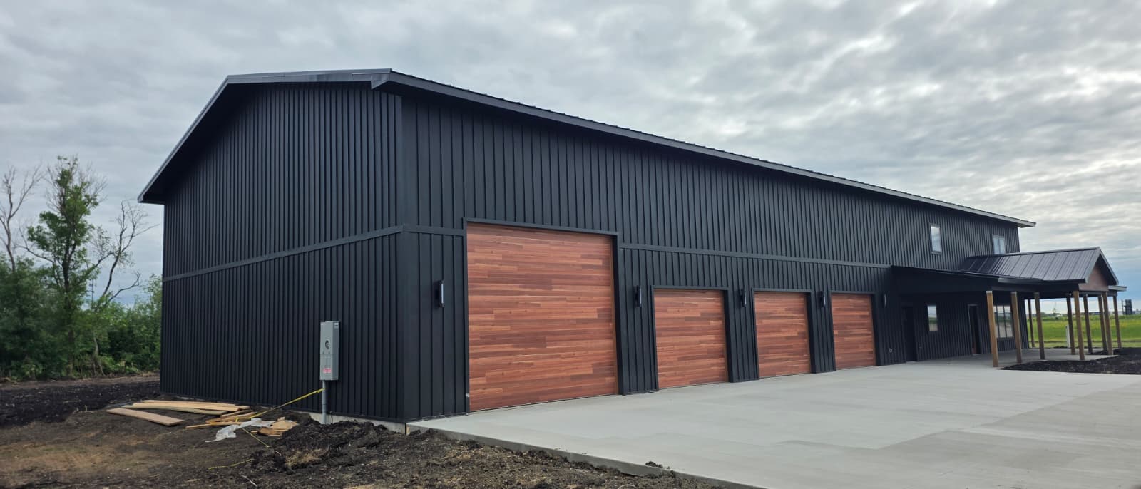 Finished Oakmont black barndominium with wood-tone doors and canopy
