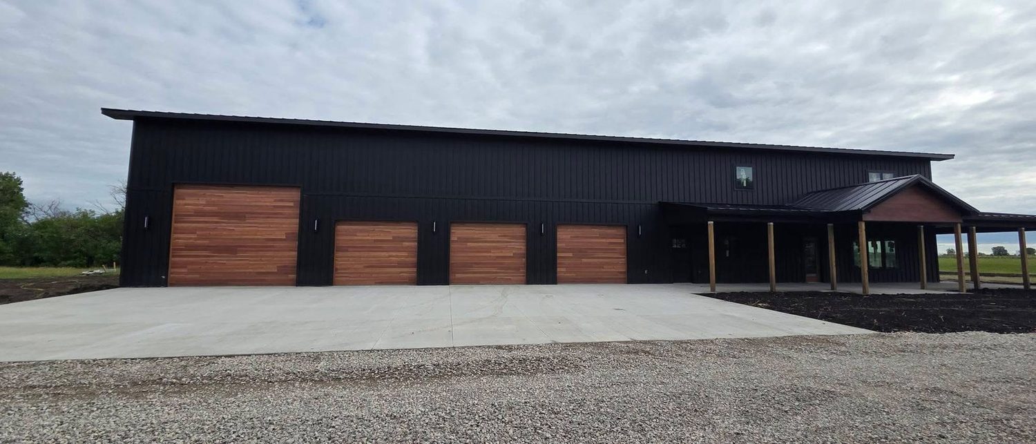 Finished Oakmont black barndominium, four wood-tone overhead doors along a black metal wall